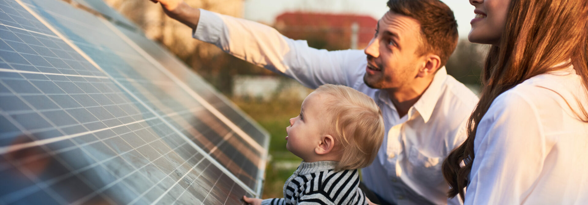Un homme, une femme et un jeune enfant observent des panneaux solaires, l’homme pointant du doigt la surface des panneaux.